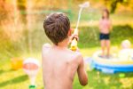 Boy splashing girl with water gun, garden swimming pool